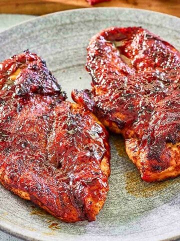 two BBQ chicken breasts on a plate.
