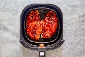 two bbq chicken breasts in an air fryer basket.