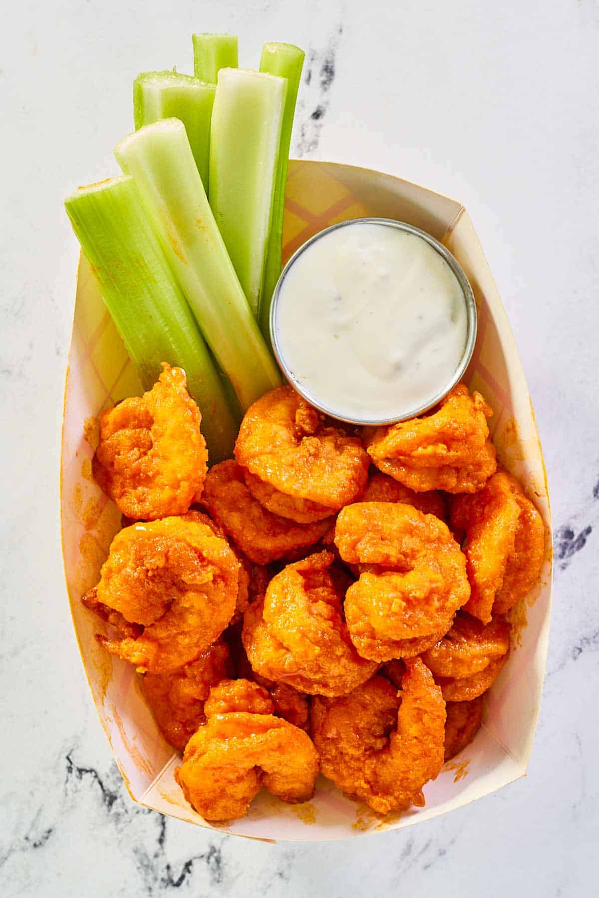 overhead view of fried buffalo shrimp, celery sticks, and dip in a paper basket.