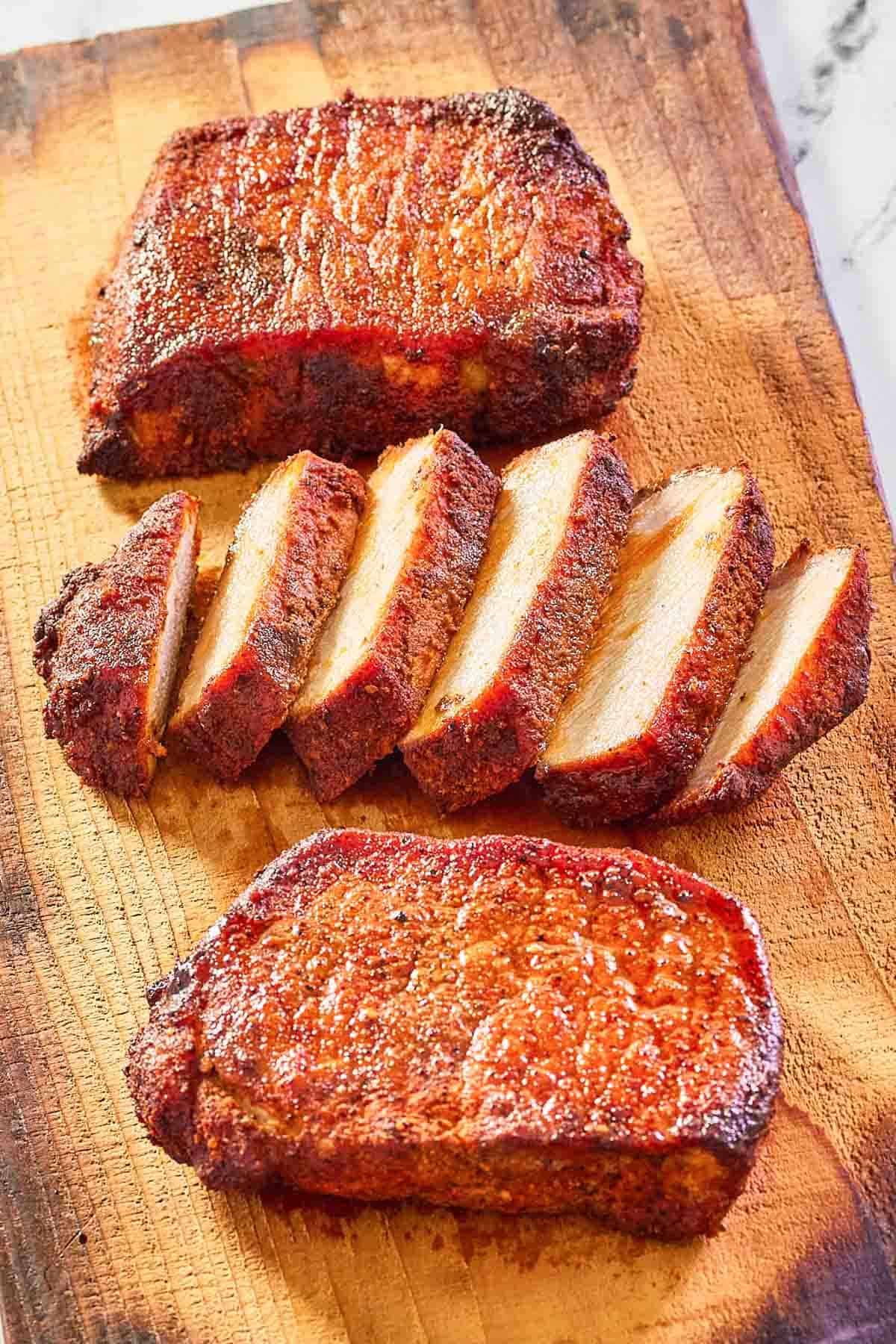 three smoked pork chops on a wood board.