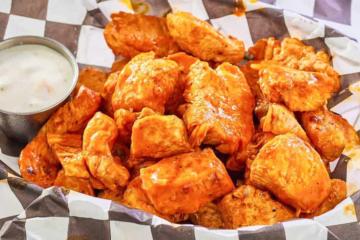 grilled buffalo chicken bites and blue cheese dressing in a parchment paper lined basket.