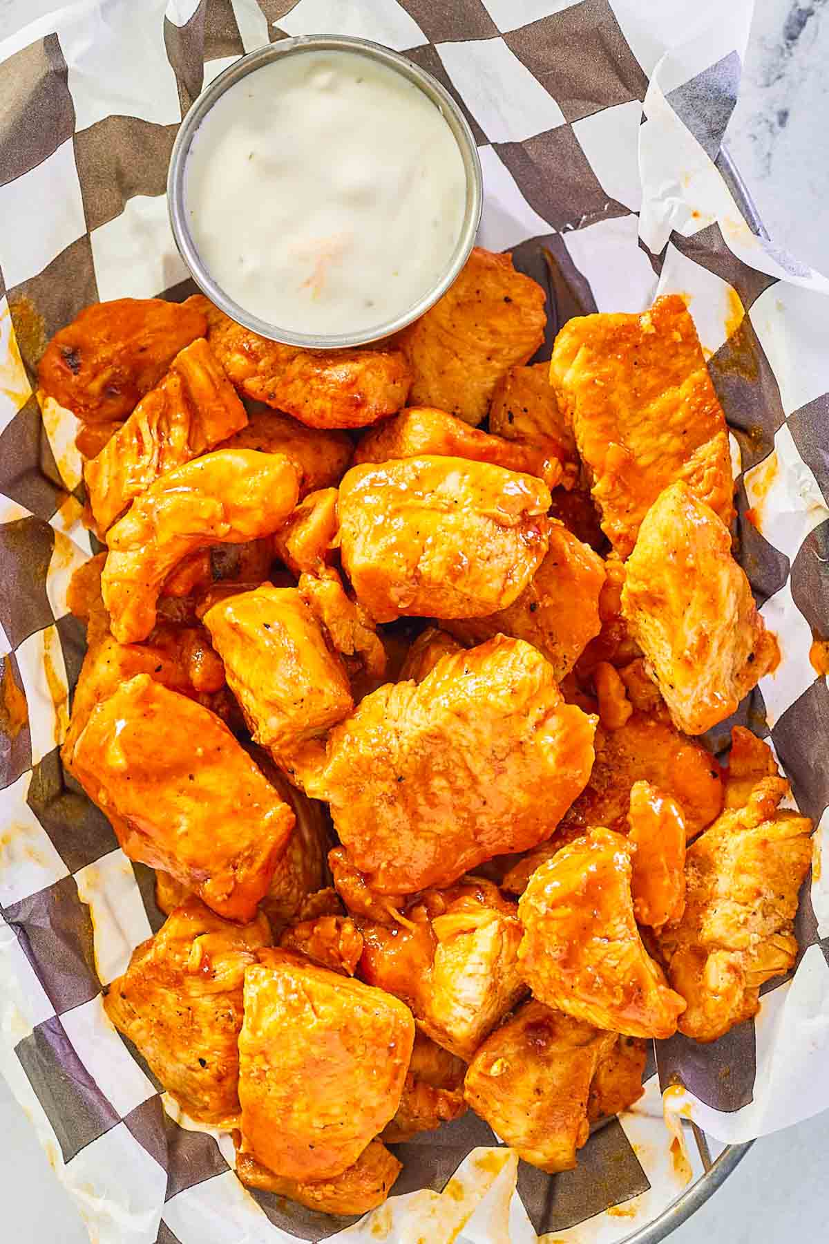 overhead view of grilled buffalo chicken bites and blue cheese dressing in a basket.