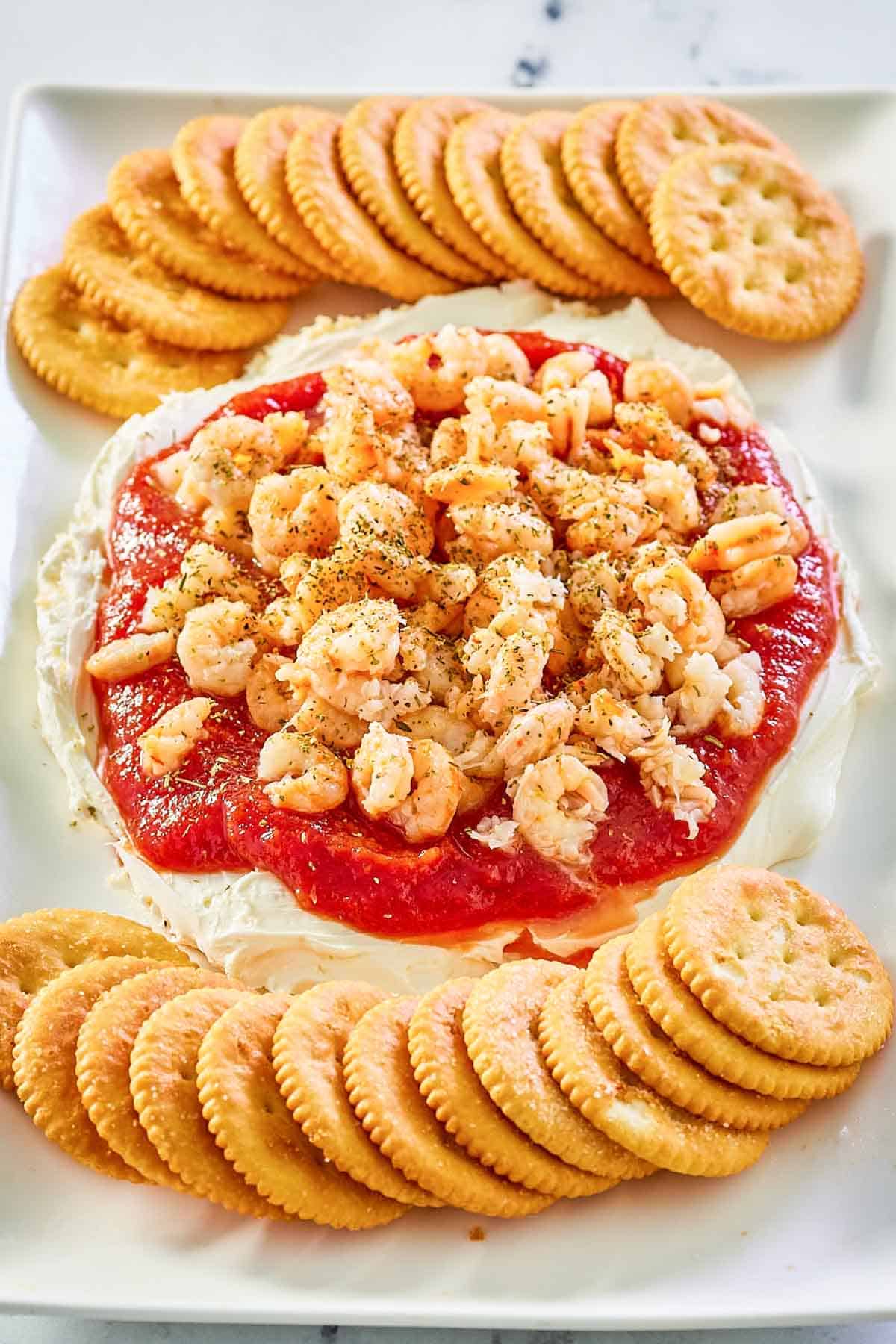 layered shrimp dip with round butter crackers on a white platter.