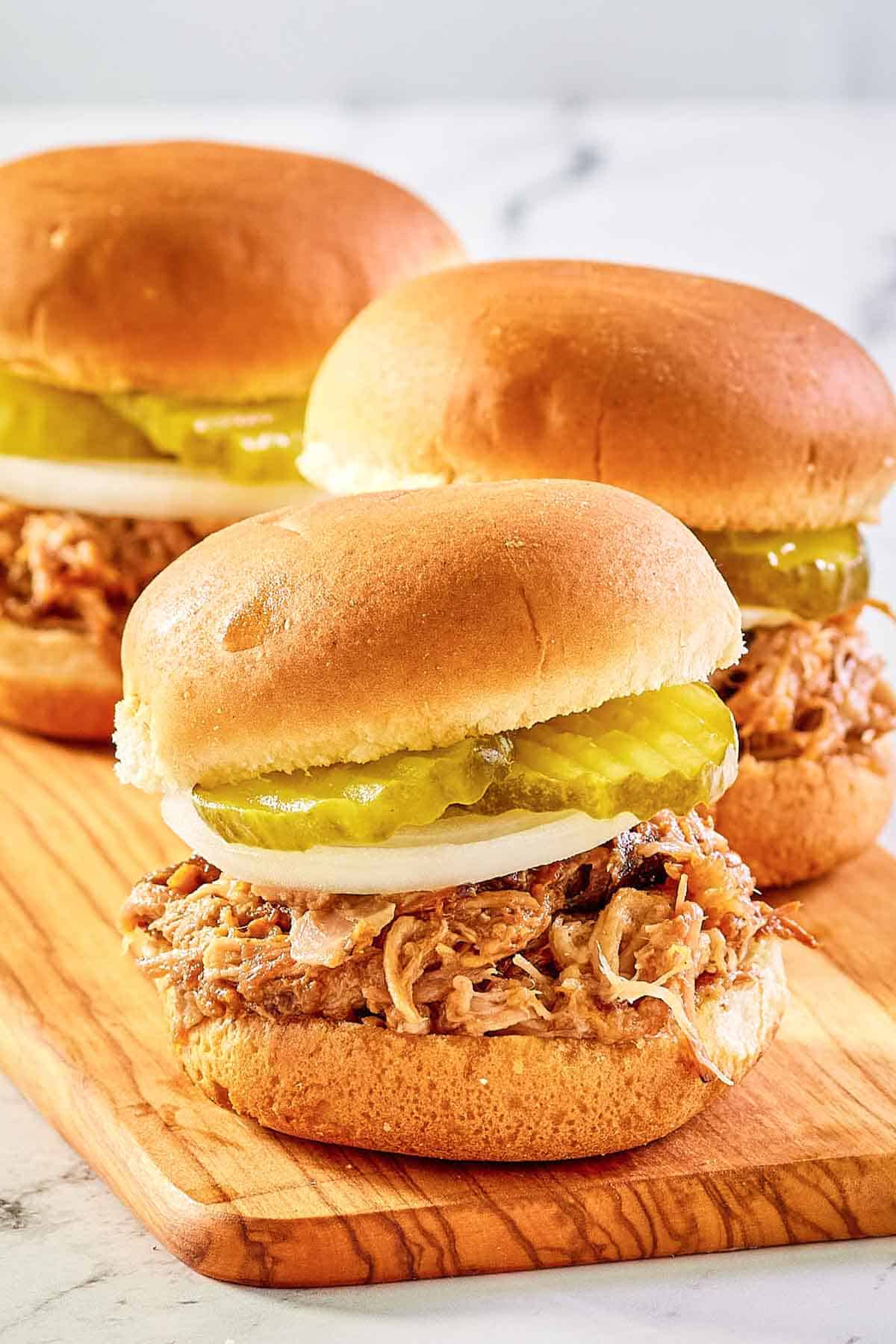 three pulled pork sliders on a wood serving board.