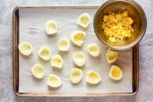 Boiled egg white halves on a baking sheet and yolks in a bowl.