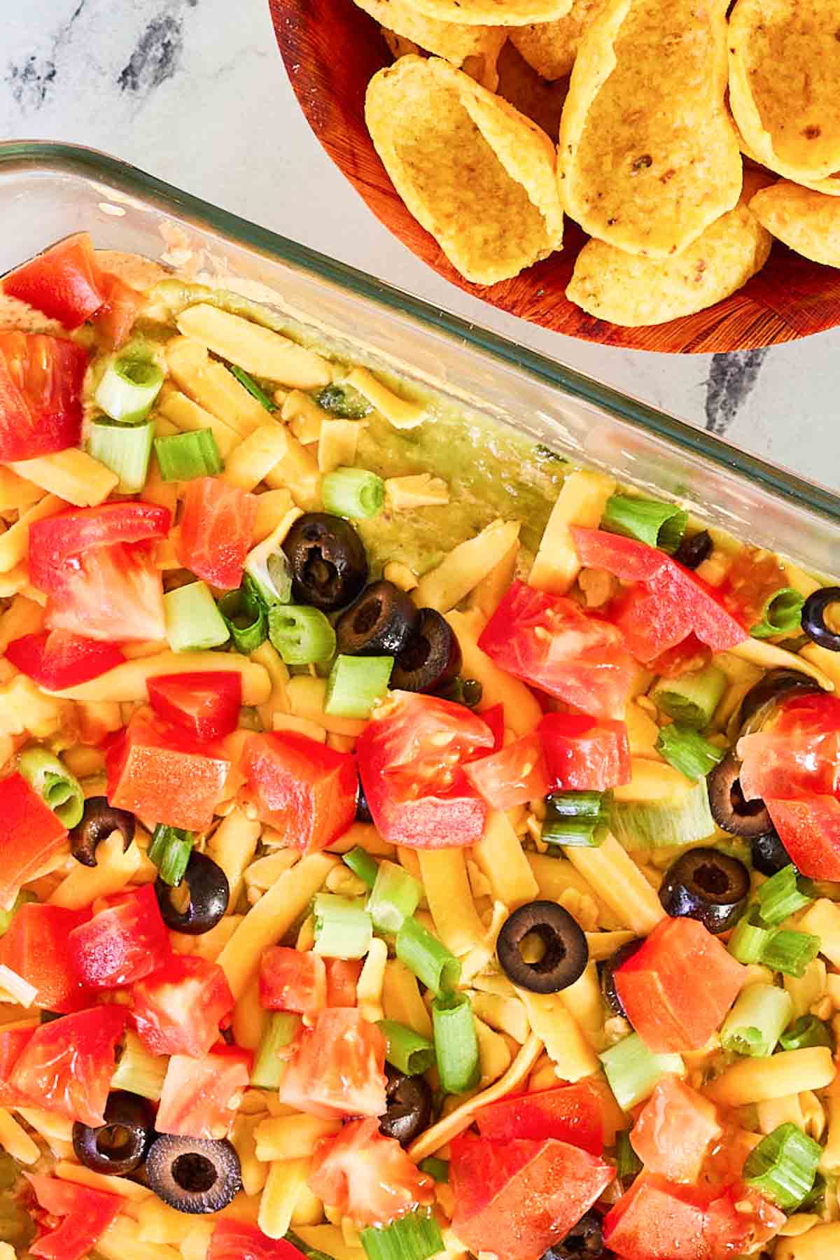 A bowl of corn chips next to taco dip with refried beans.