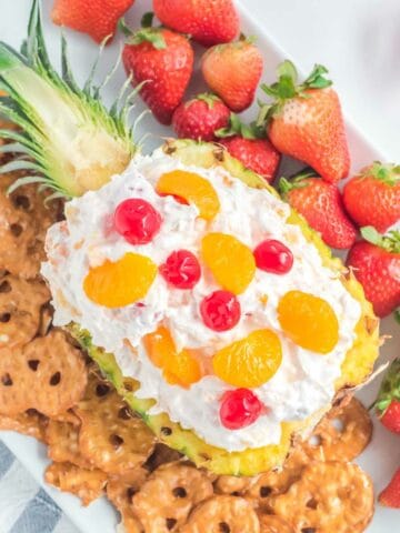 Pina colada fruit dip in a pineapple, strawberries, and pretzel chips on a platter.