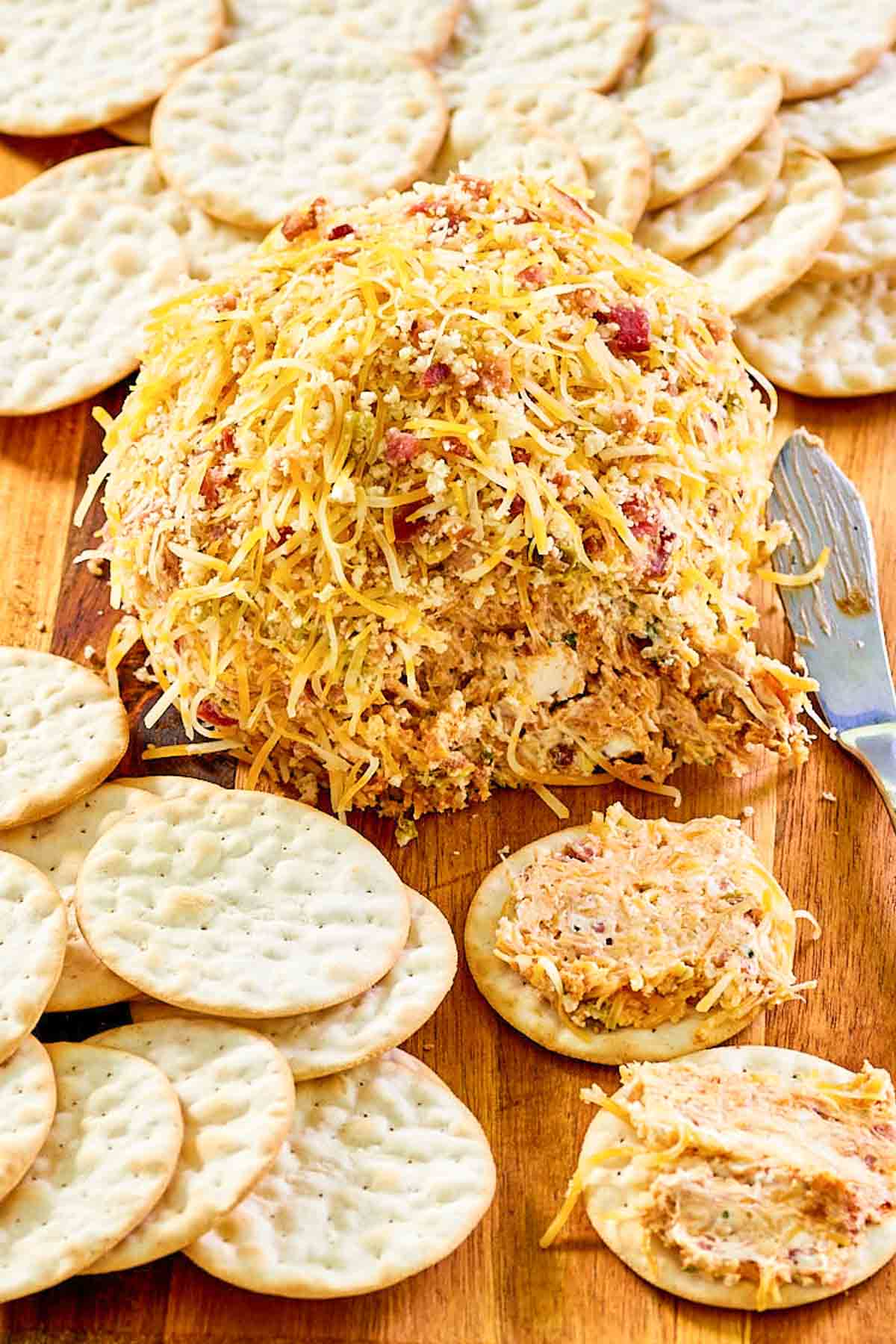 Jalapeno popper cheese ball with bacon and crackers on a wood board.