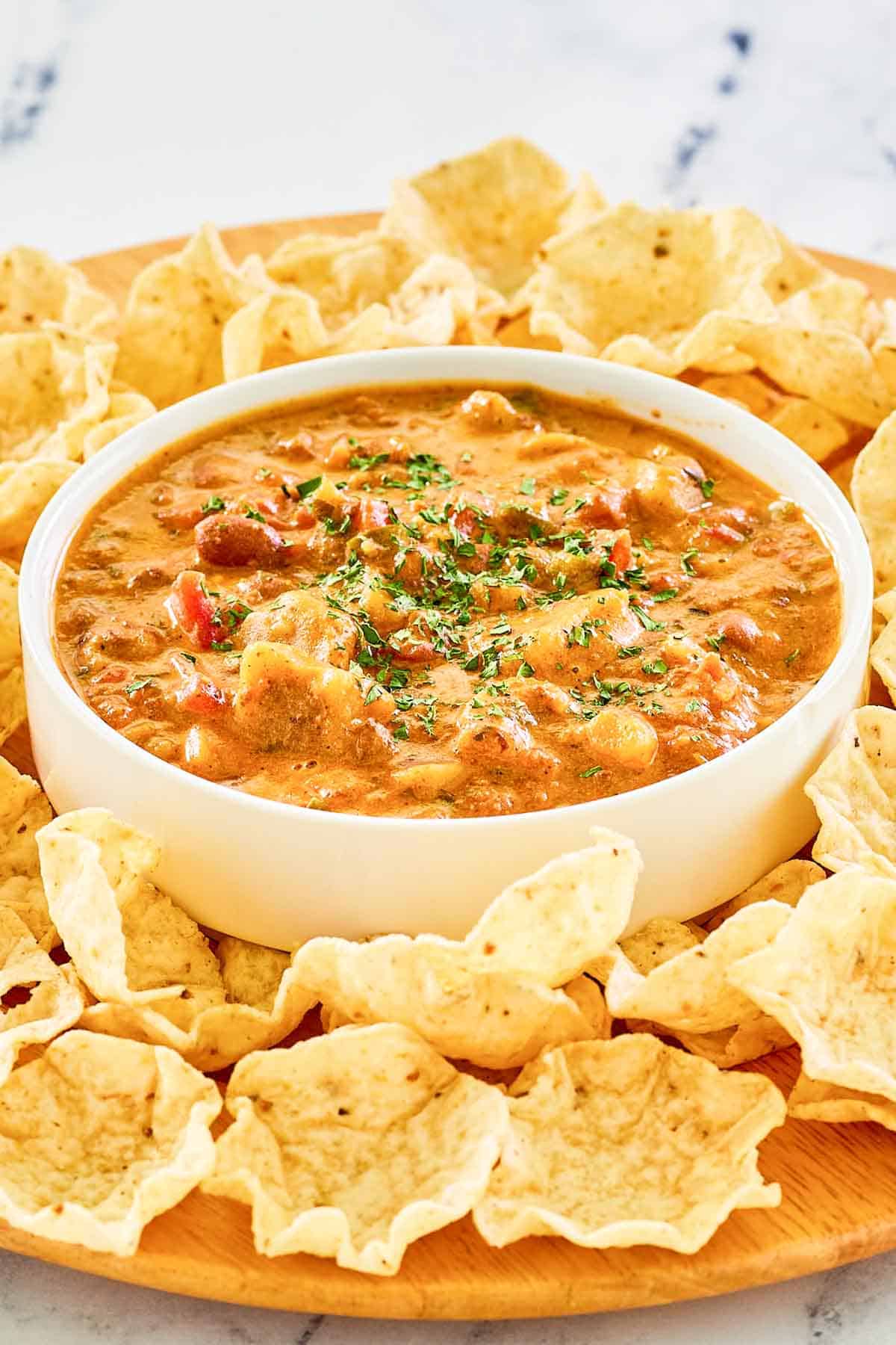A bowl of tamale dip and tortilla chips on a wood platter.