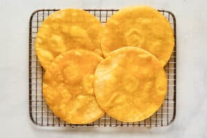 Cooked corn tortillas on a wire rack.