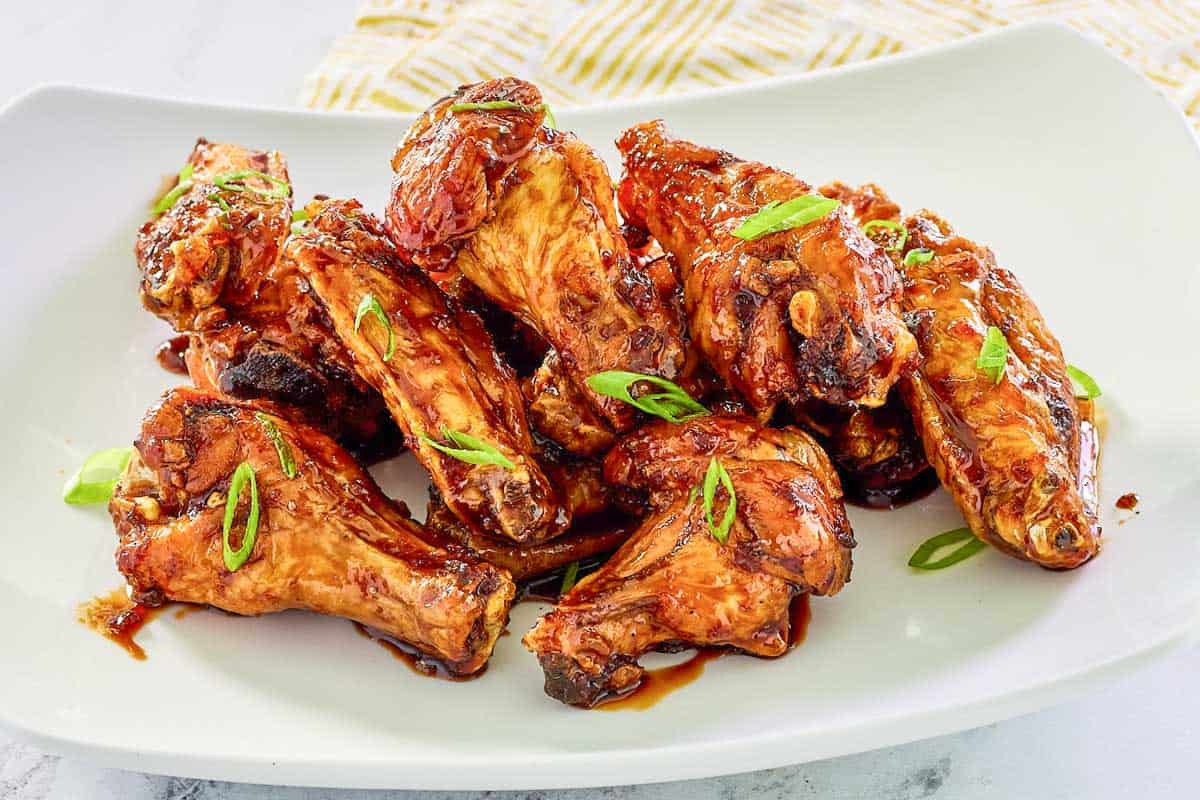 Honey garlic chicken wings garnished with green onions on a plate.