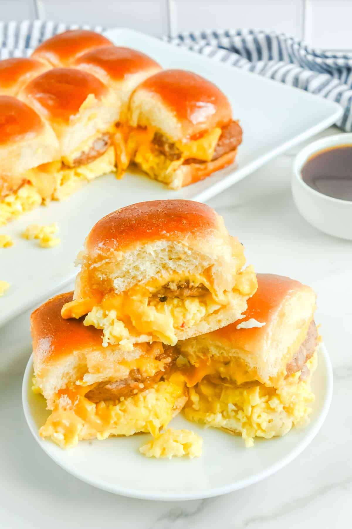 Hawaiian roll breakfast sliders on a plate and platter and a bowl of maple syrup.