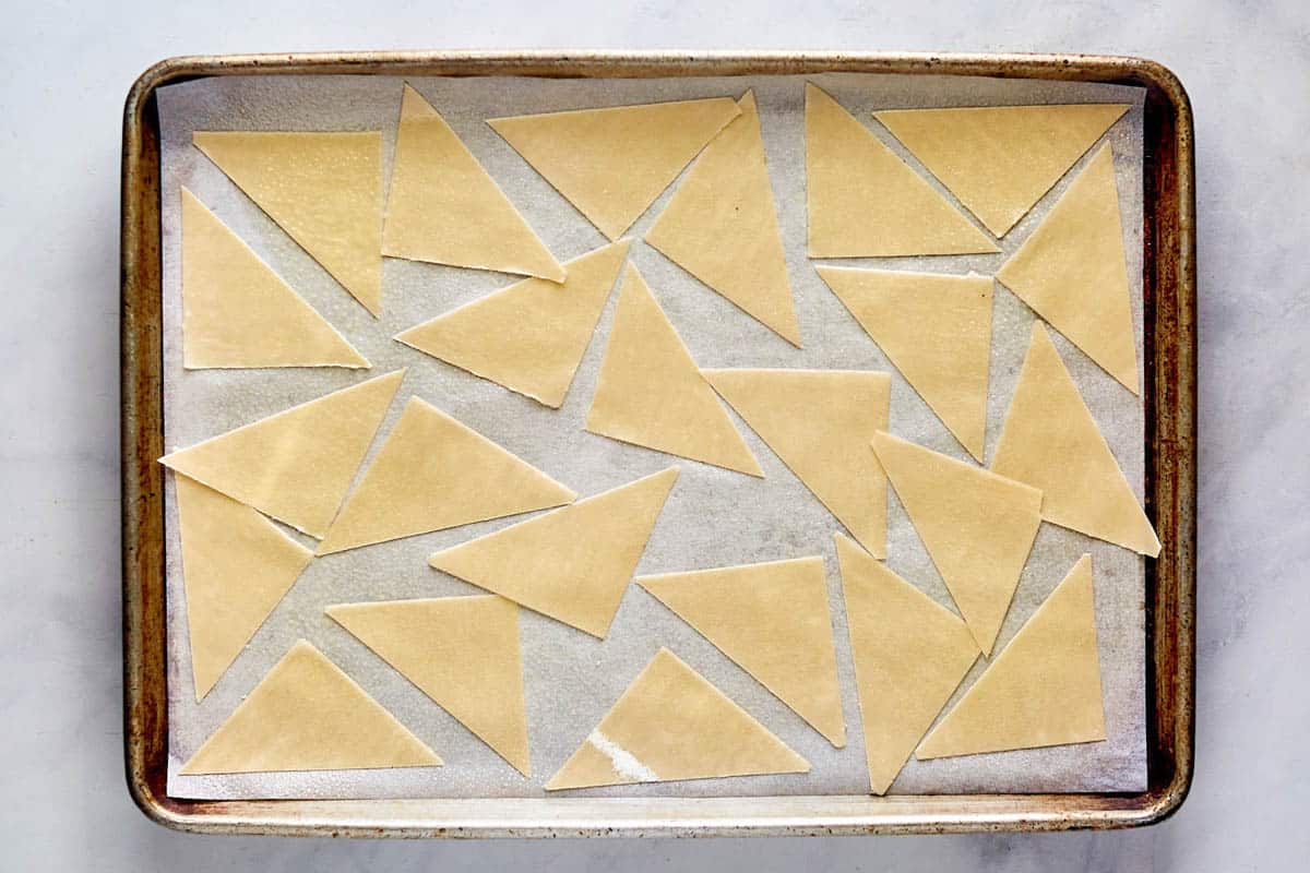 Wonton wrappers cut into triangles and on a baking sheet.