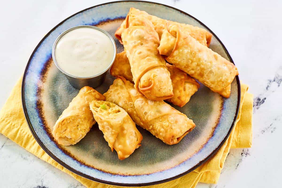 Buffalo chicken egg rolls and a small cup of dipping sauce on a large plate.