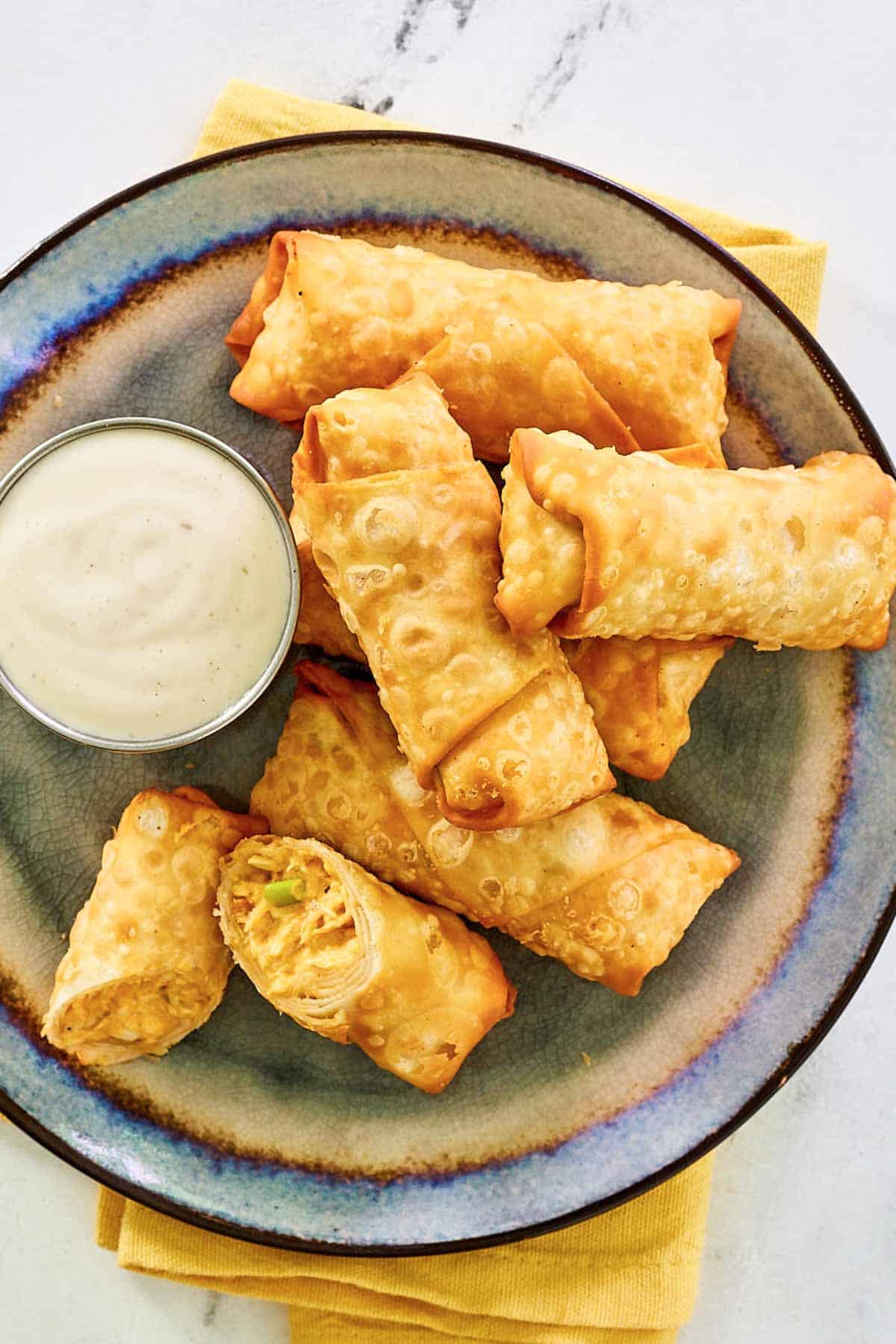 Buffalo chicken egg rolls and dipping sauce on a plate.