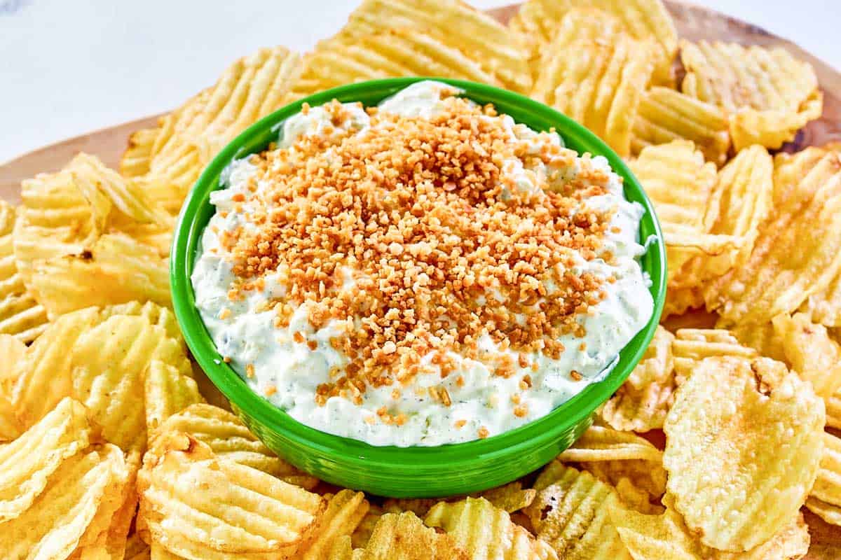A bowl of fried pickle dip and potato chips on a platter.