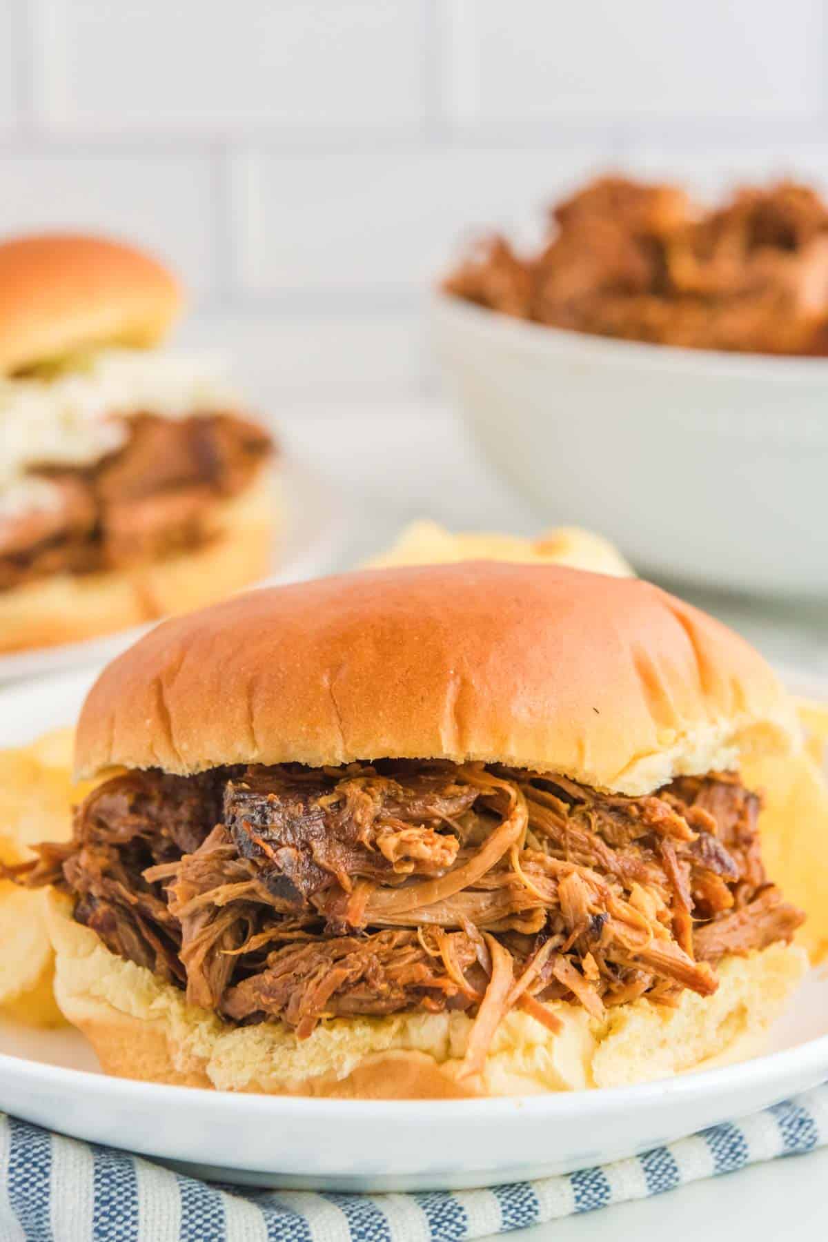 Slow cooker BBQ pulled pork sandwich and potato chips on a plate.