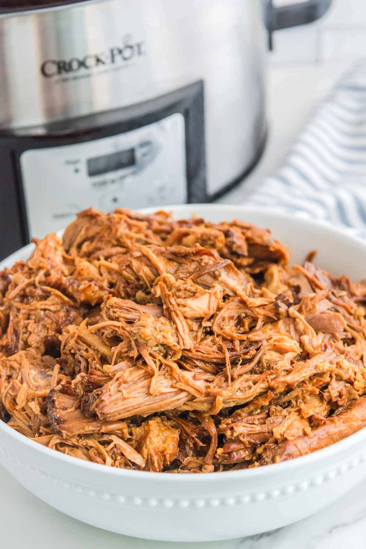 Slow cooker pulled pork with BBQ sauce in a bowl and a Crockpot.