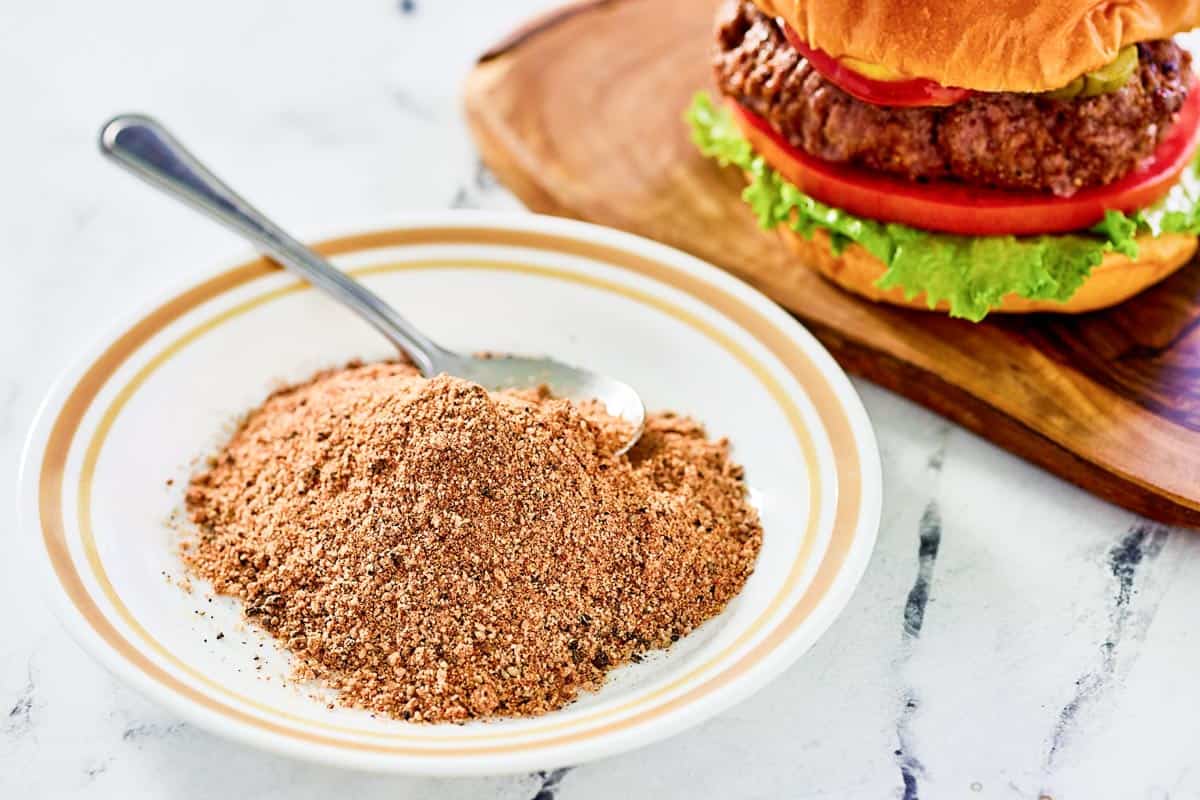 A bowl of homemade burger seasoning for grilling and a burger next to it.