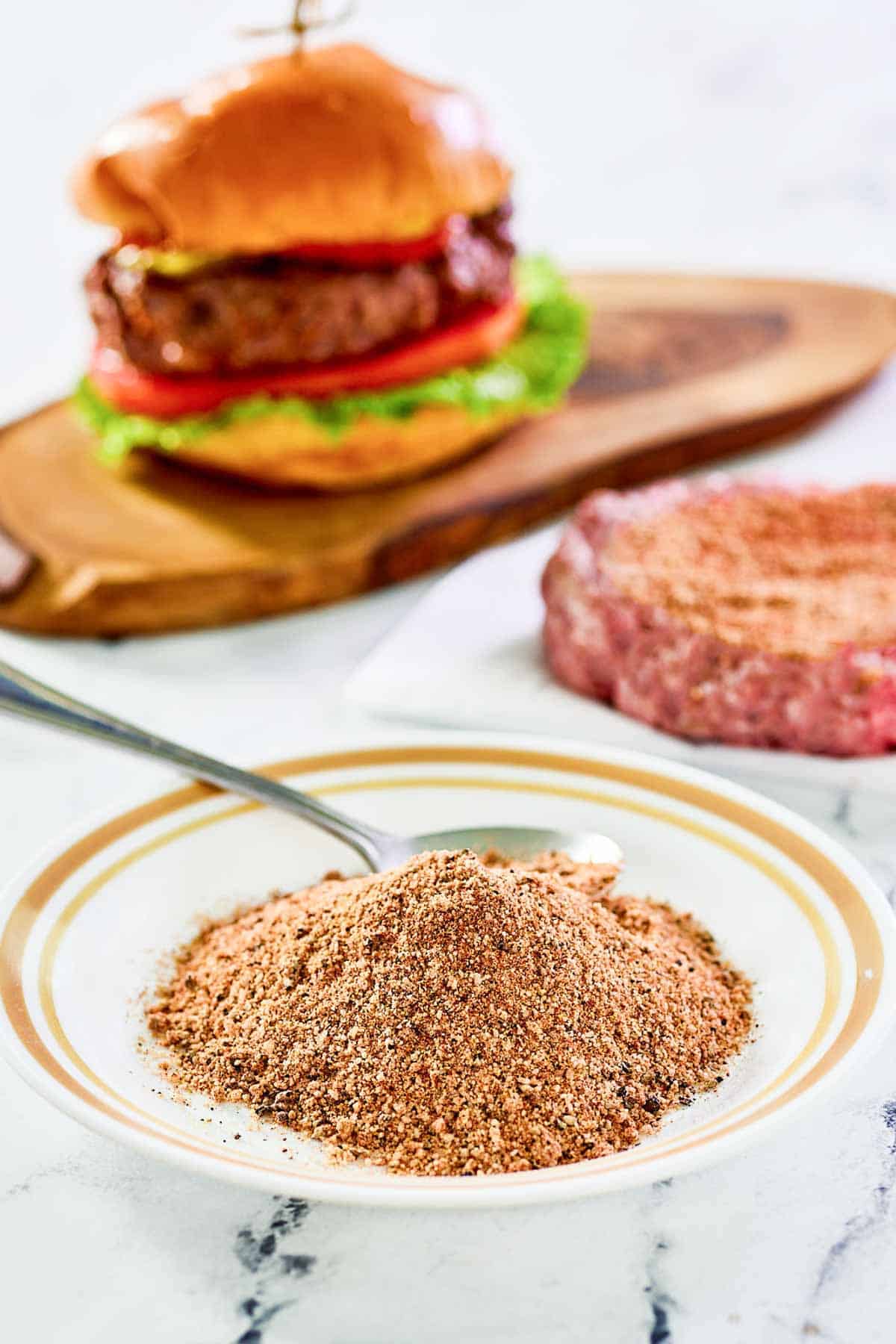 Homemade burger seasoning for grilling on a small plate and a burger behind it.