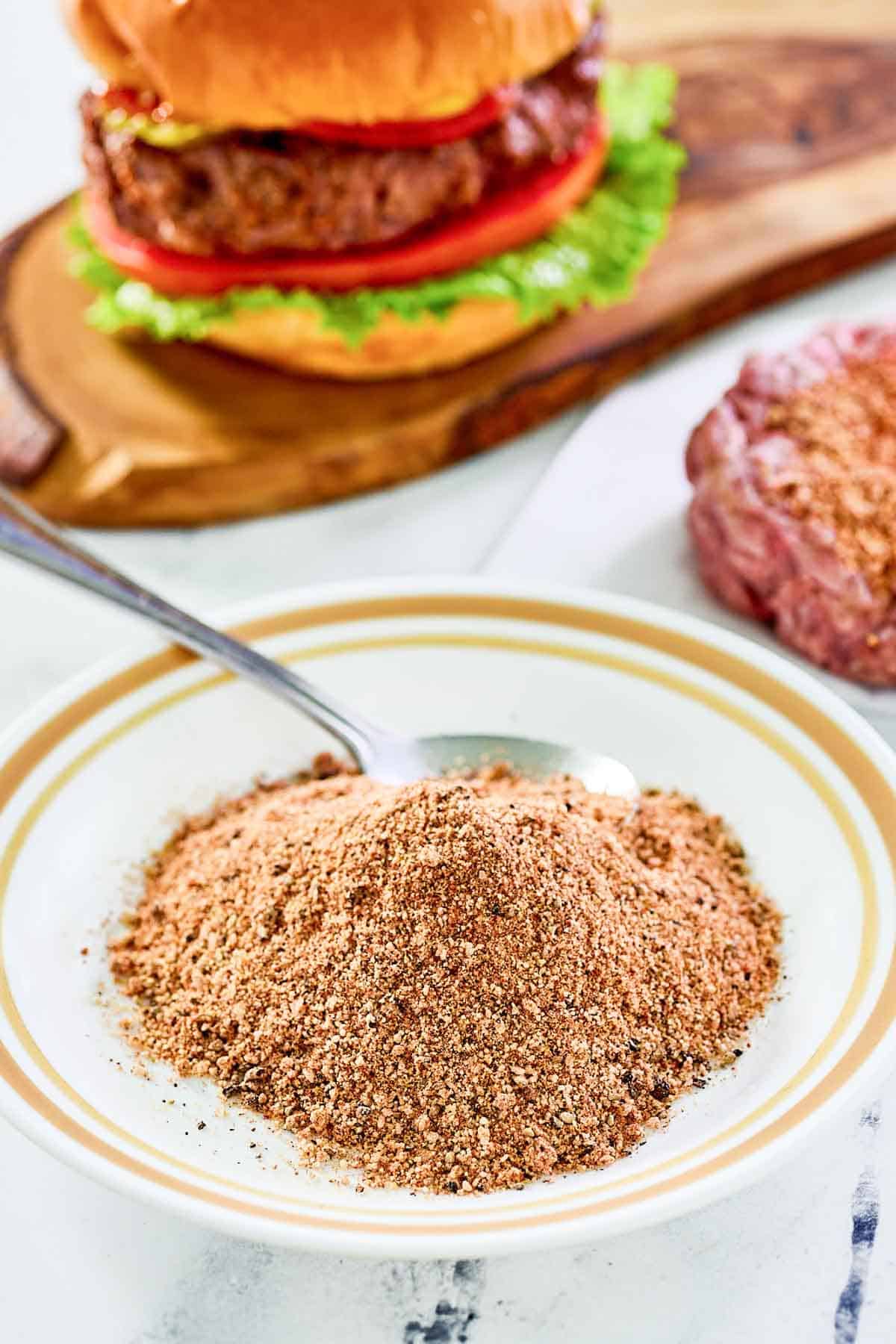 A bowl of homemade burger seasoning for grilling and a burger behind it.