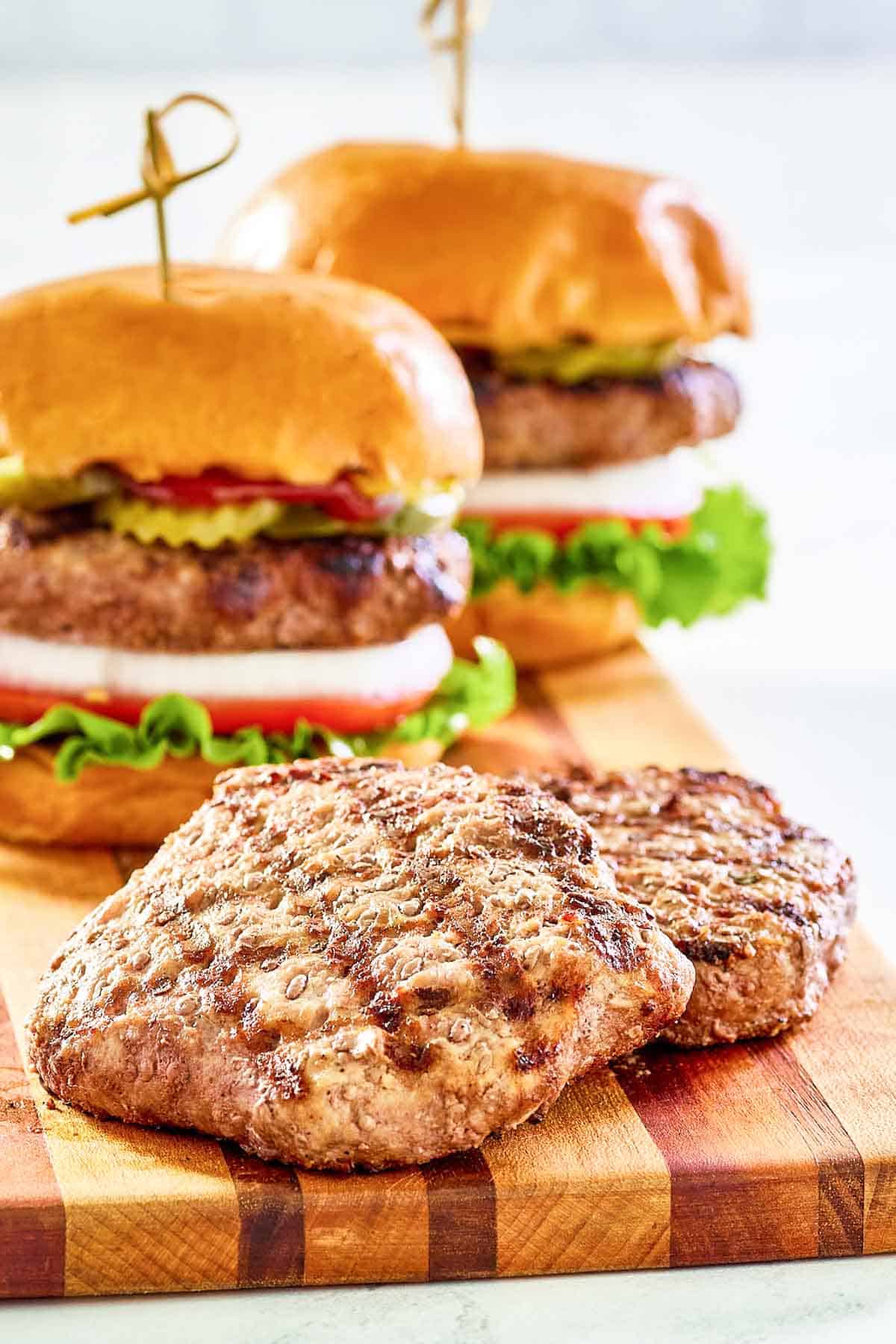Grilled frozen burger patties and burgers on a wood board.