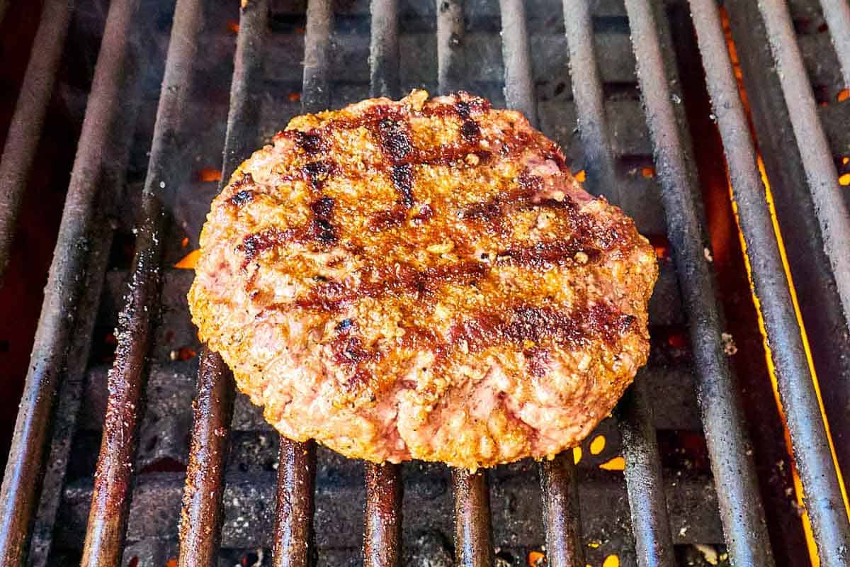 Grilled burger patty with homemade burger seasoning on a grill grate.