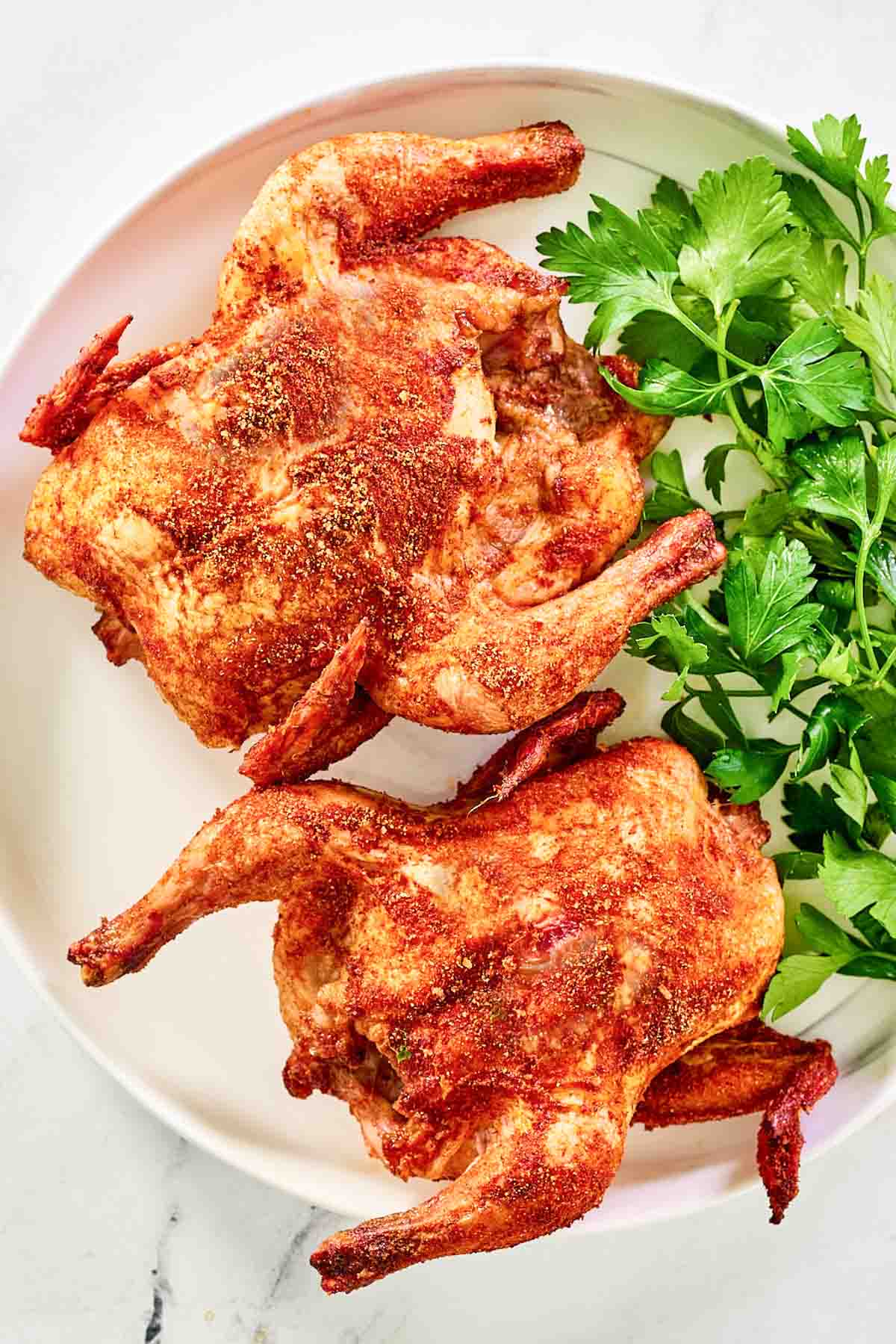 Two smoked cornish hens and parsley on a platter.