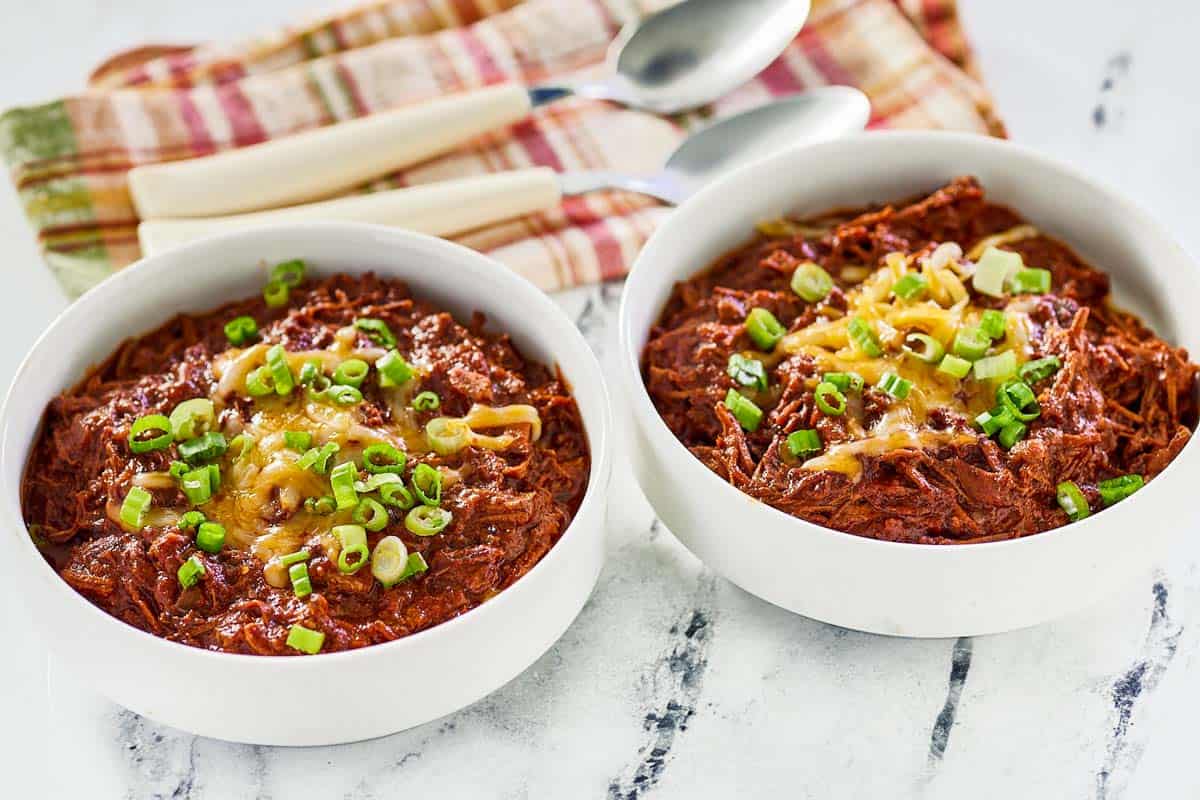 Brisket chili topped with cheese and green onions in two bowls.