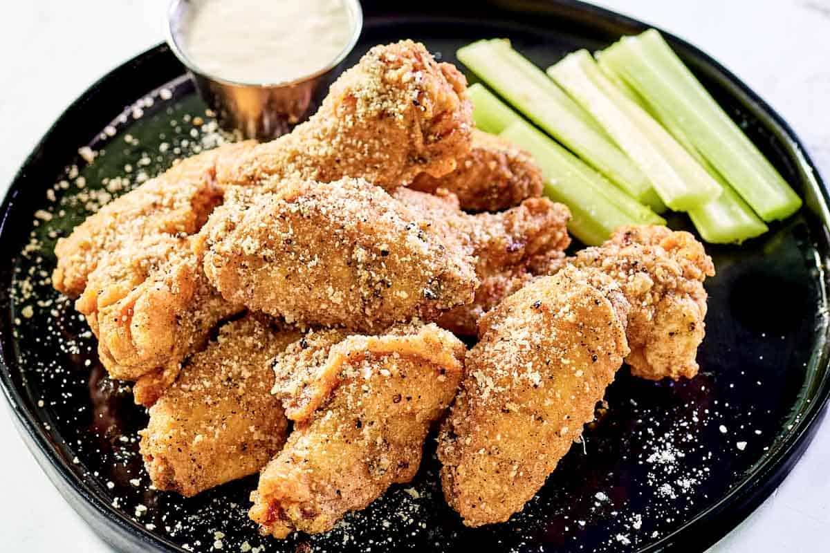 Breaded garlic parmesan wings, dipping sauce, and celery sticks on a plate.