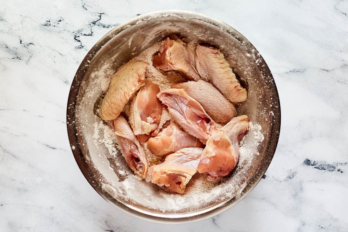 Raw chicken wings and seasoned flour in a bowl.