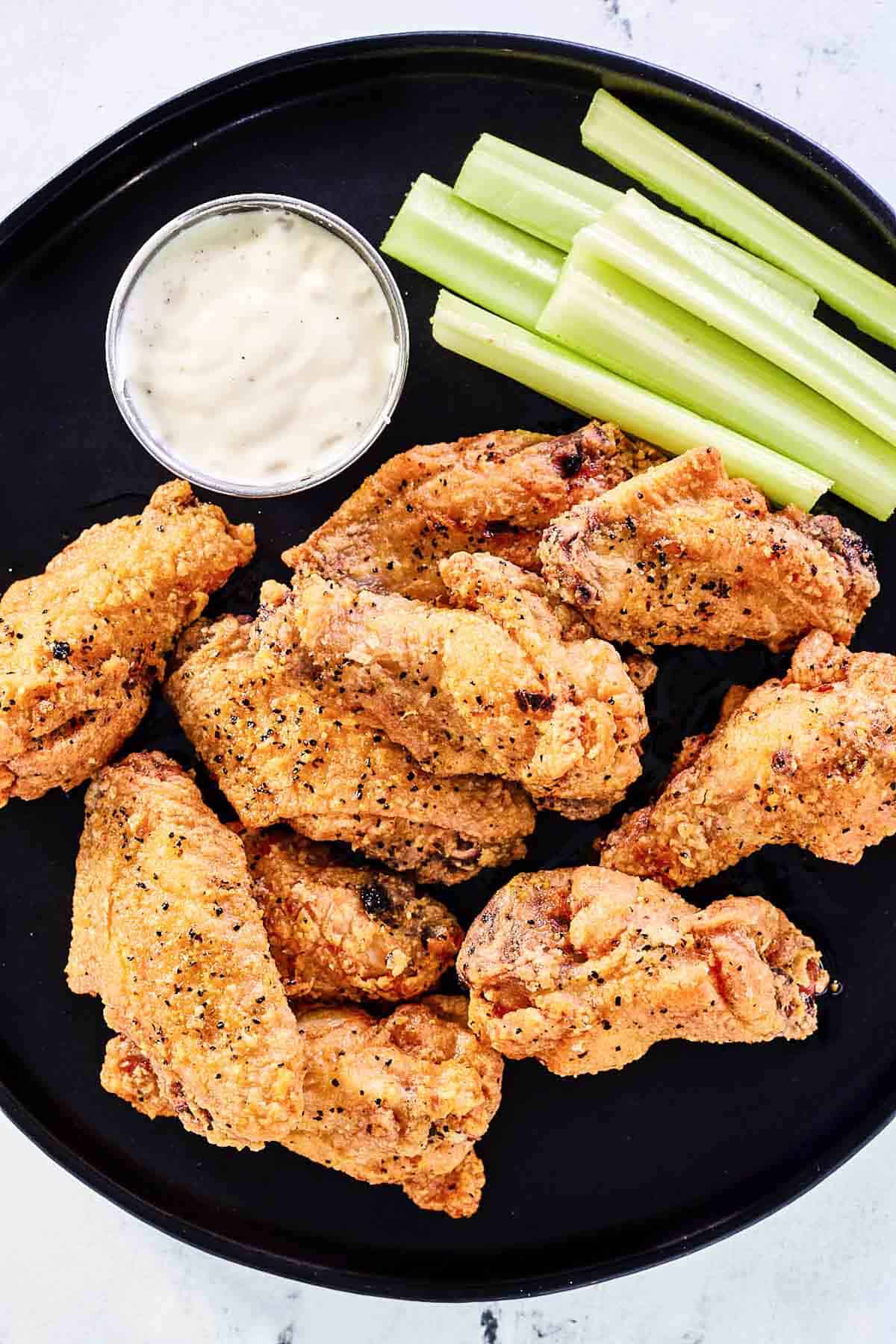 Breaded lemon pepper wings, celery sticks, and dipping sauce on a plate.