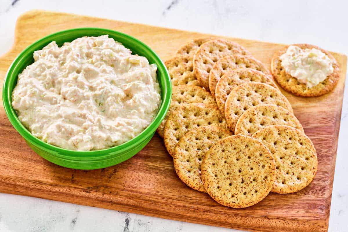 Pepperoncini dip and wheat crackers on a wood serving board.