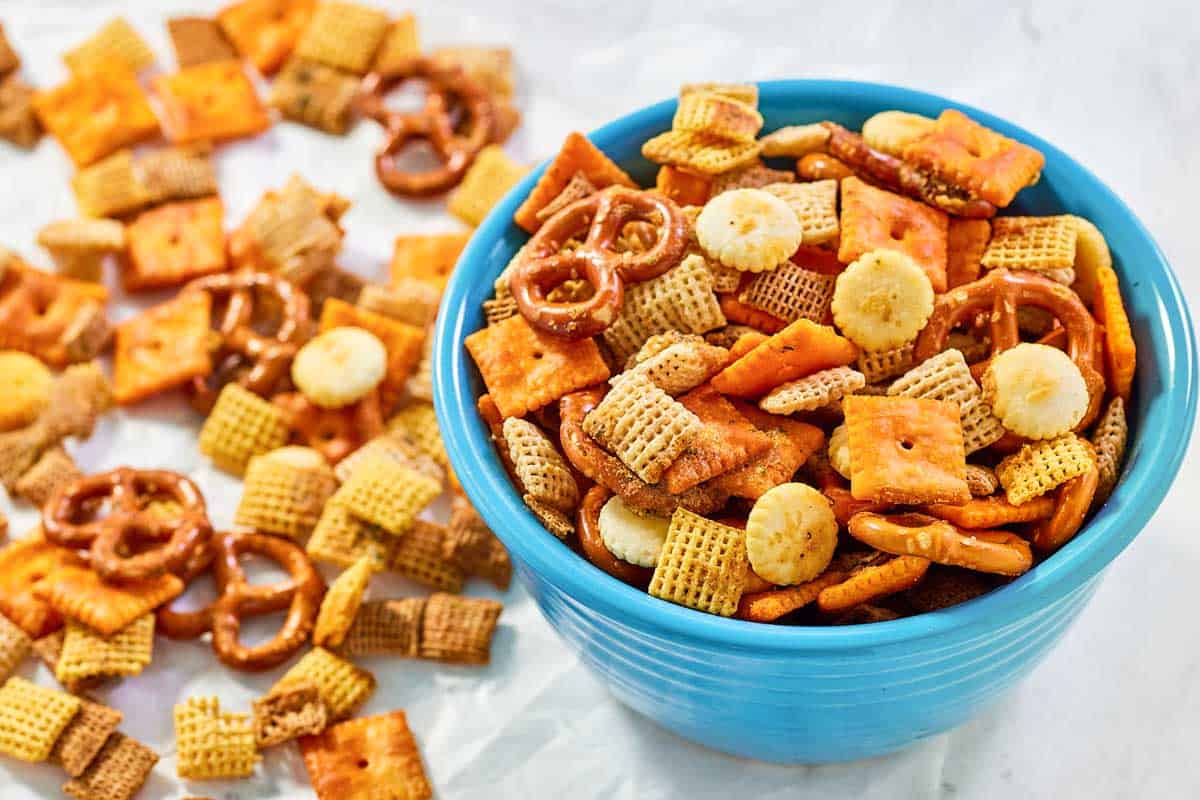 Cheesy ranch chex mix in a bowl and beside it on parchment paper.