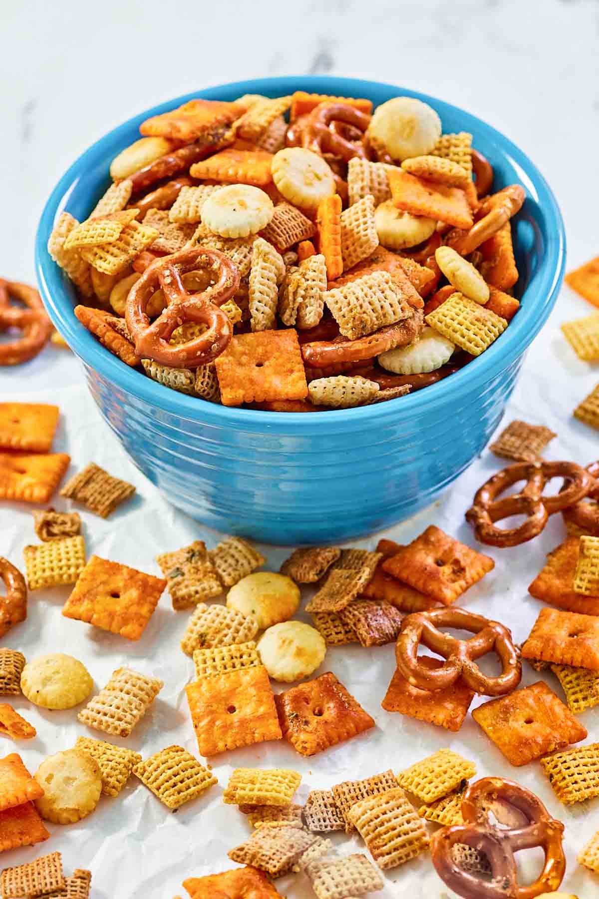 Homemade cheesy ranch chex mix in a bowl and scattered in front of it.
