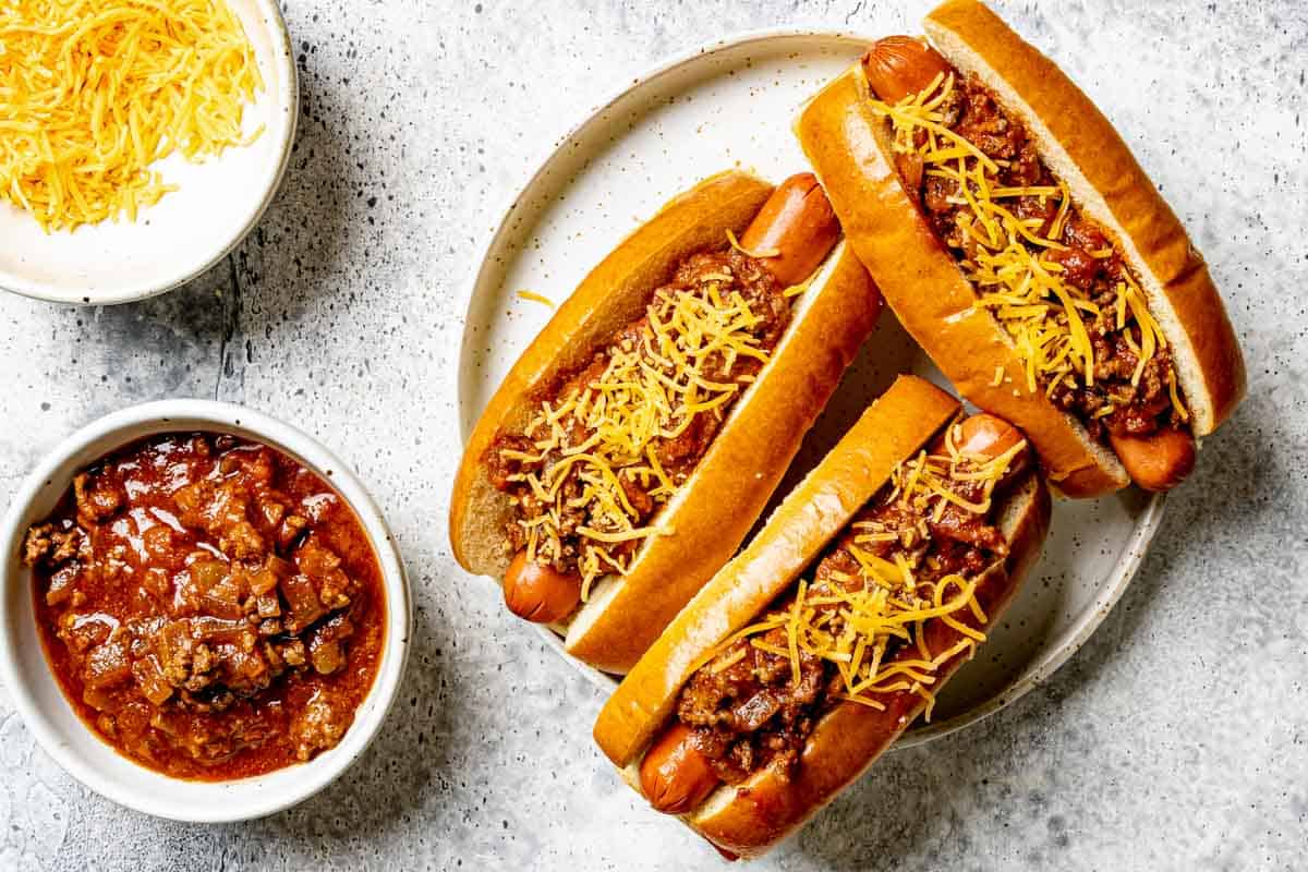 Homemade hot dog chili in a bowl and on top of three hot dogs.