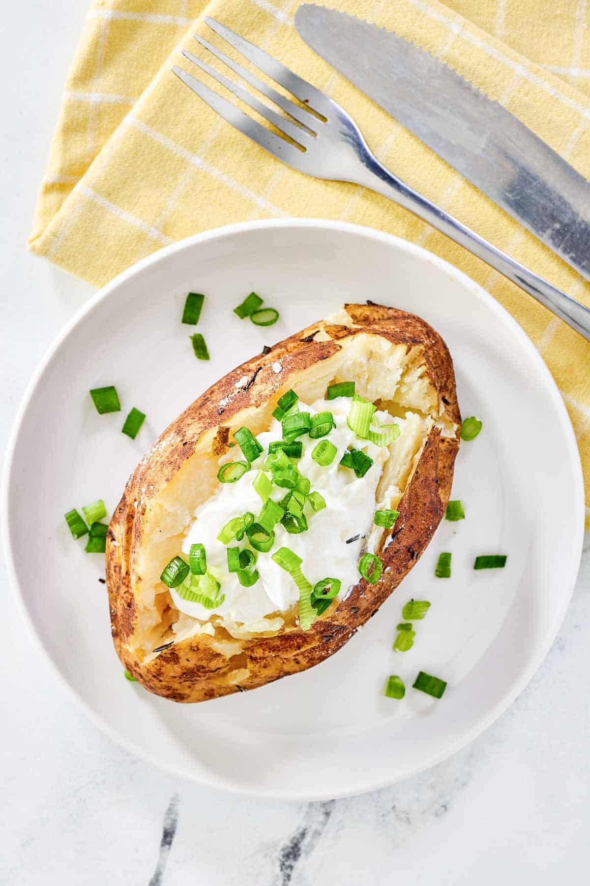 Grilled baked potato on a plate and a knife and fork on a cloth napkin.