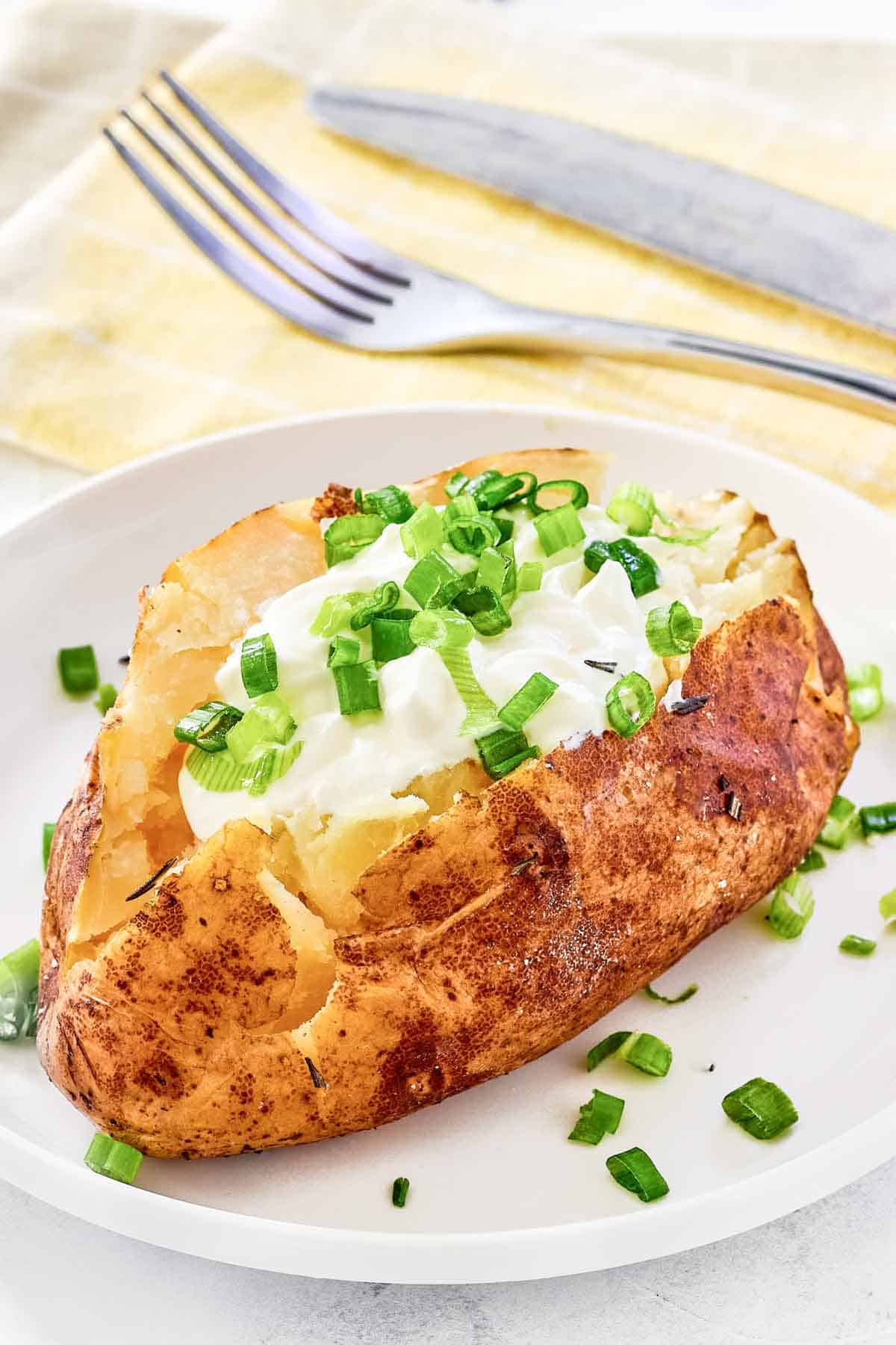 Grilled baked potato with toppings on a plate and a knife and fork on a napkin.