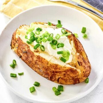 Grilled baked potato with toppings on a plate.