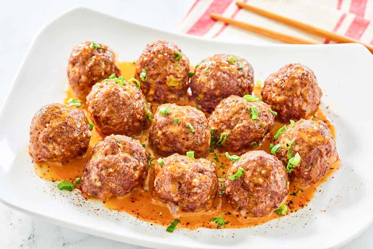 Firecracker meatballs with sauce on a rectangular plate.