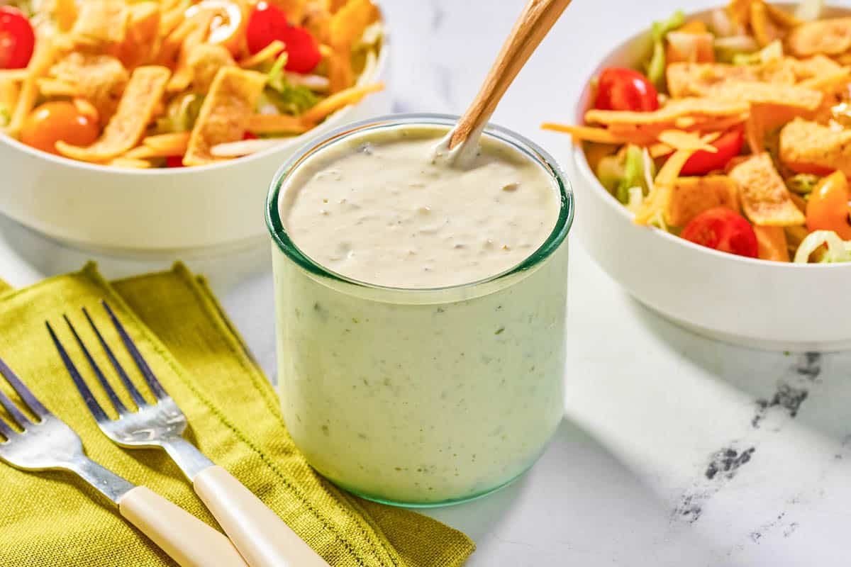 Homemade jalapeno ranch dressing in a glass jar and two salads.