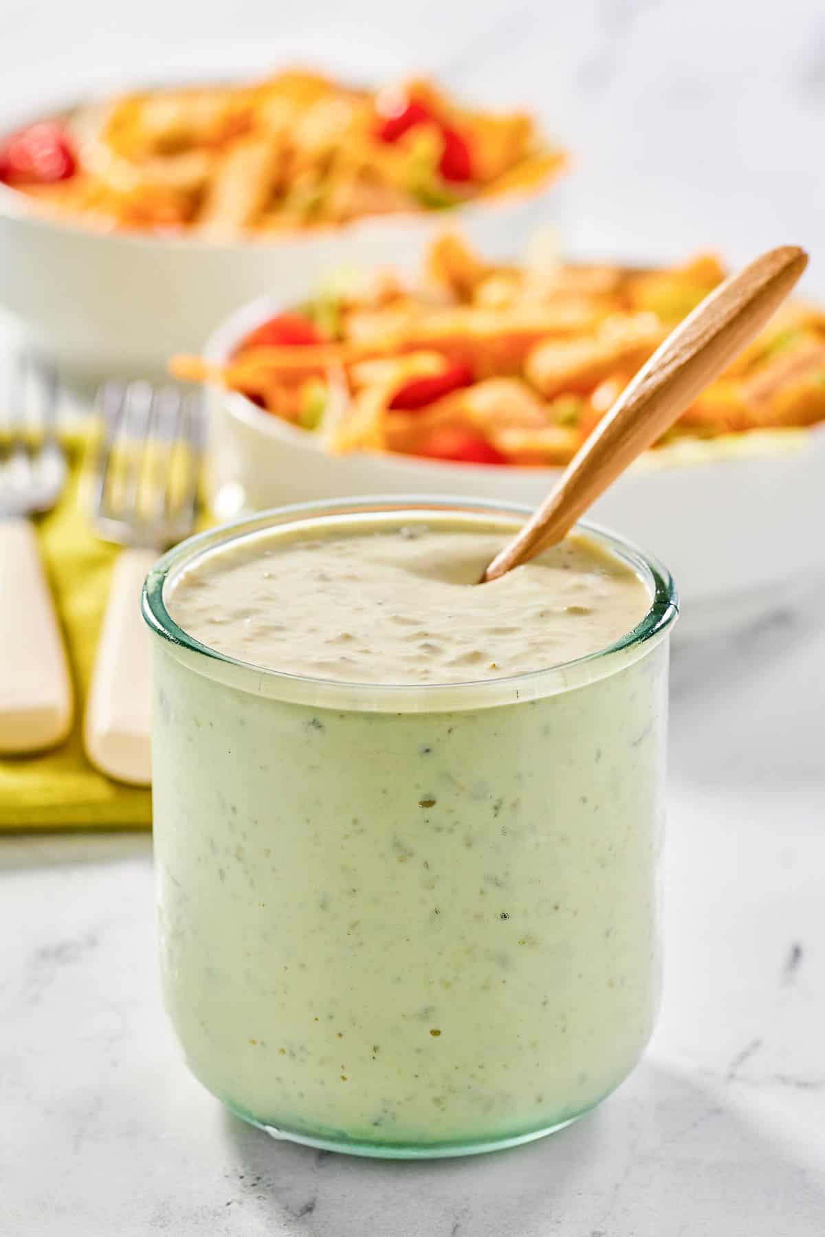 Homemade jalapeno ranch dressing a jar and two salads behind it.