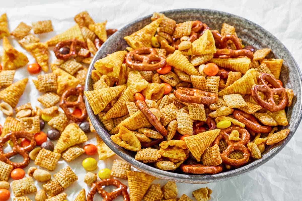 Sweet and salty chex mix on parchment paper next to a bowl of the mix.