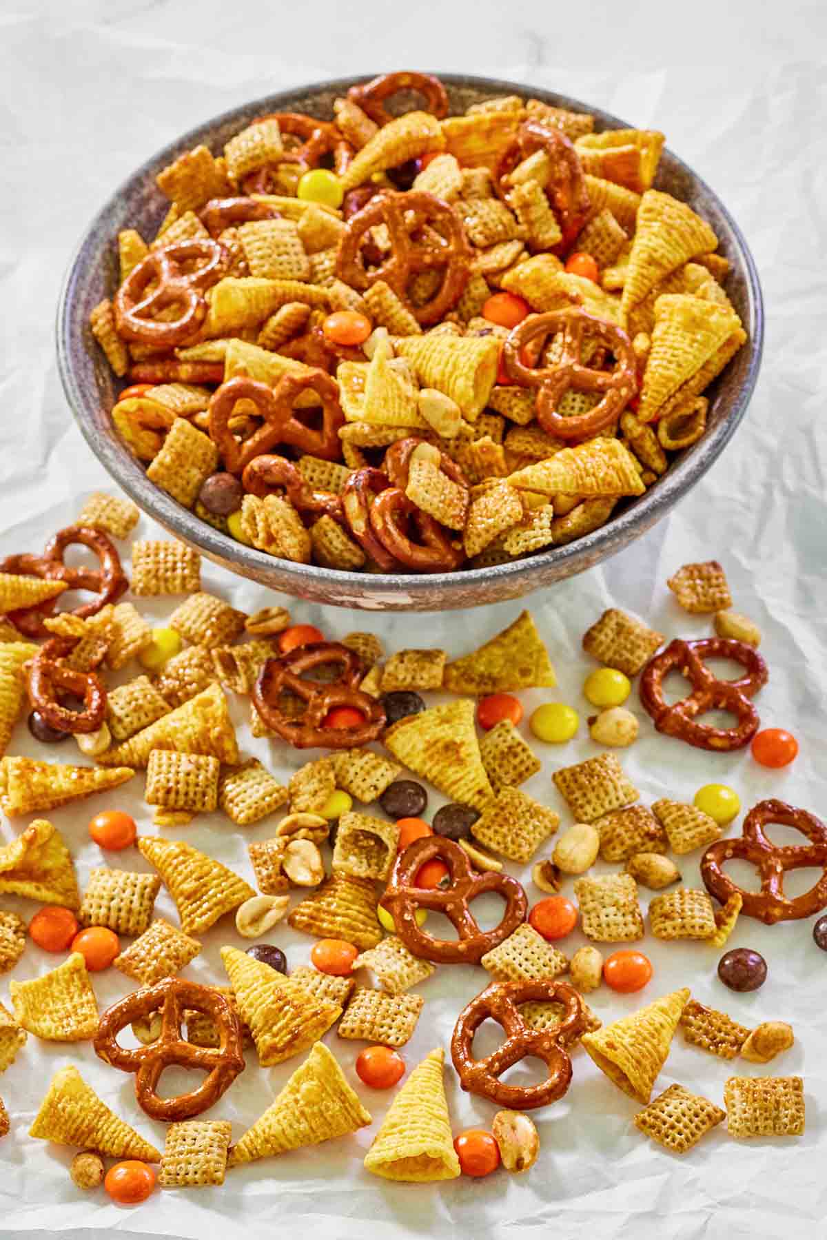 Sweet and salty Chex mix in a bowl and on parchment paper in front of the bowl.