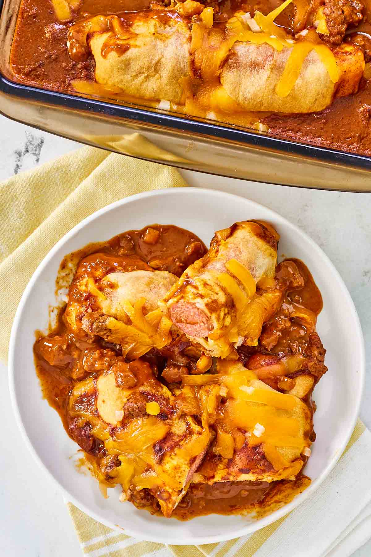 Chili dog casserole in a glass baking dish and a serving on a plate.